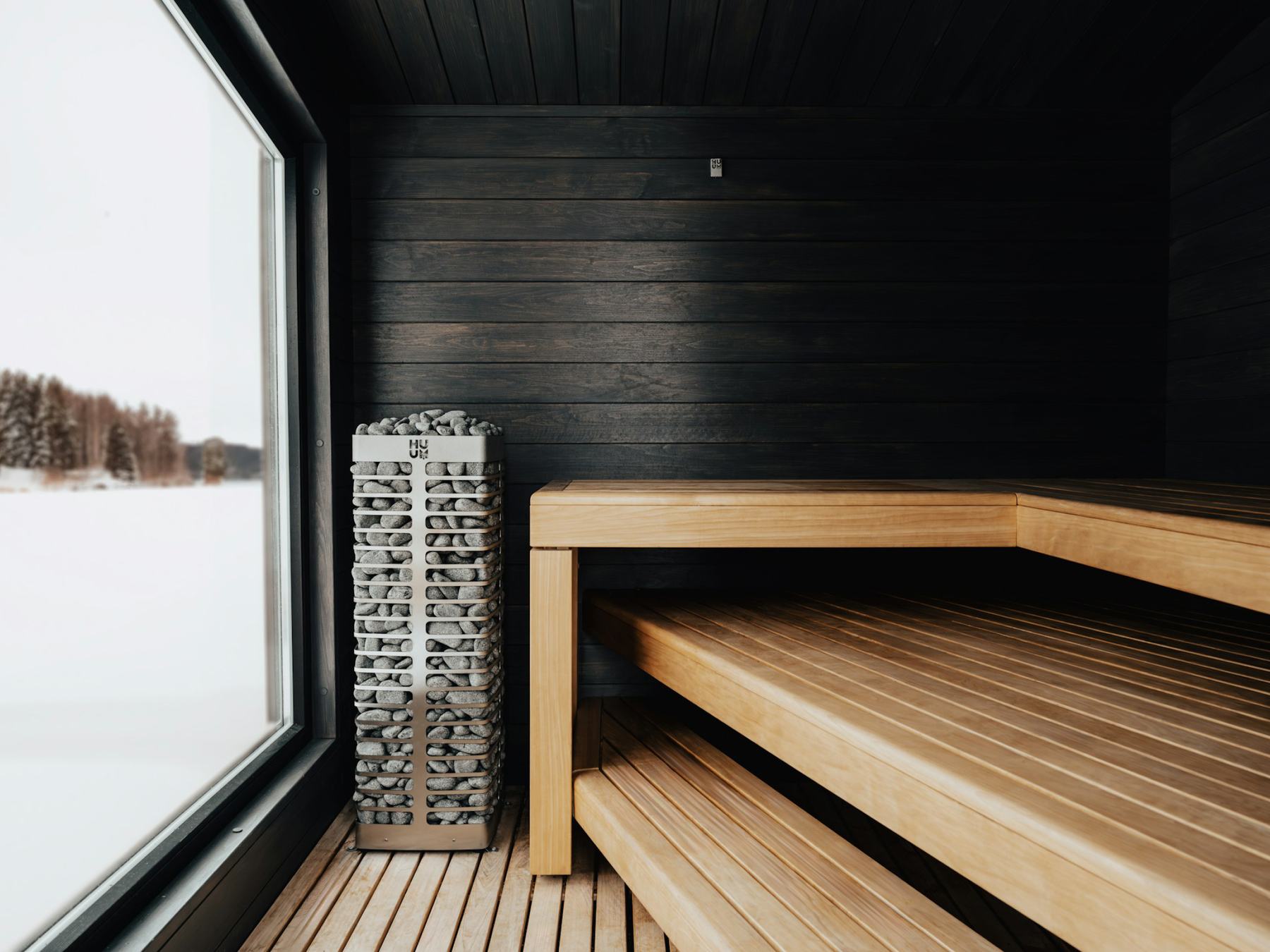 A dark sauna with black walls and a window onto snow