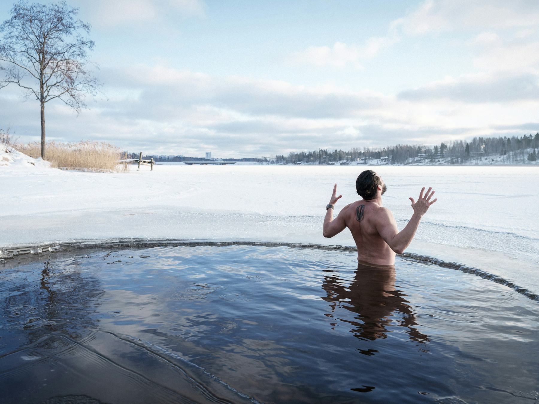 A man standing chest-deep in an ice pool cut into the frozen harbour