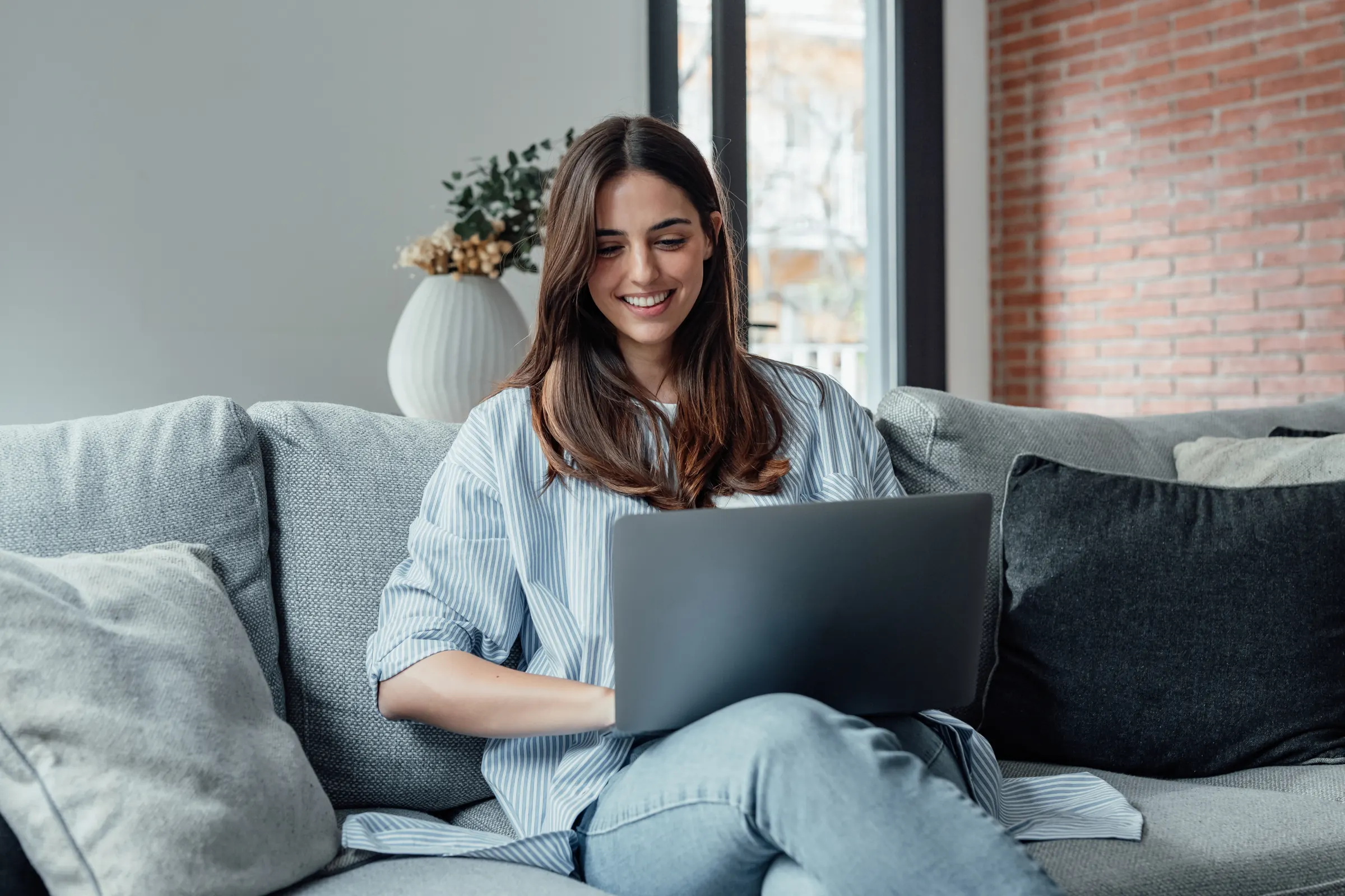 Young woman smiling at her laptop on a sofa