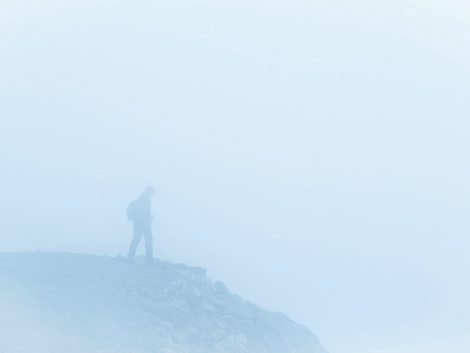 A hiker standing on a ridge in thick fog