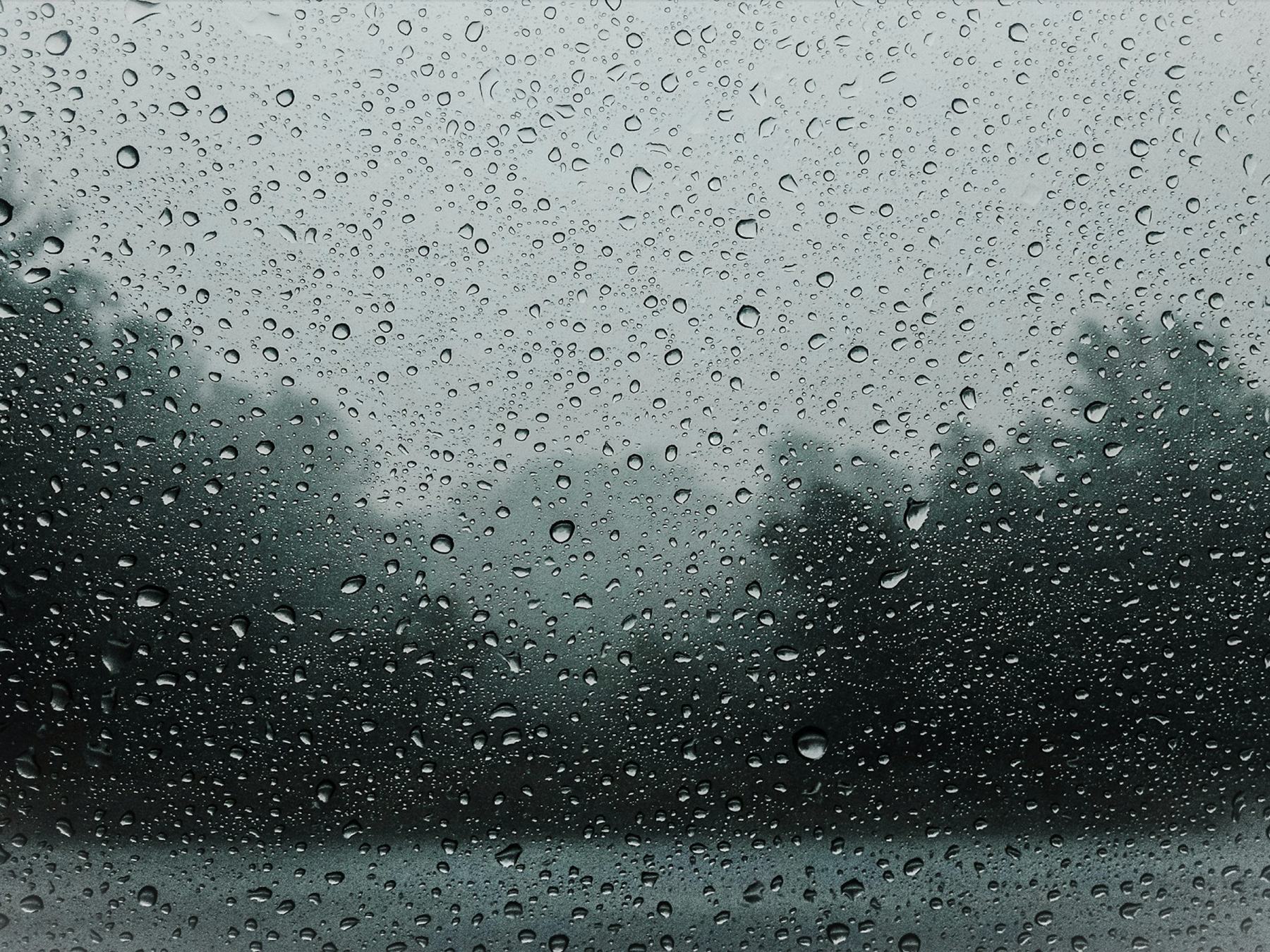 Heavy rain on a window in front of trees