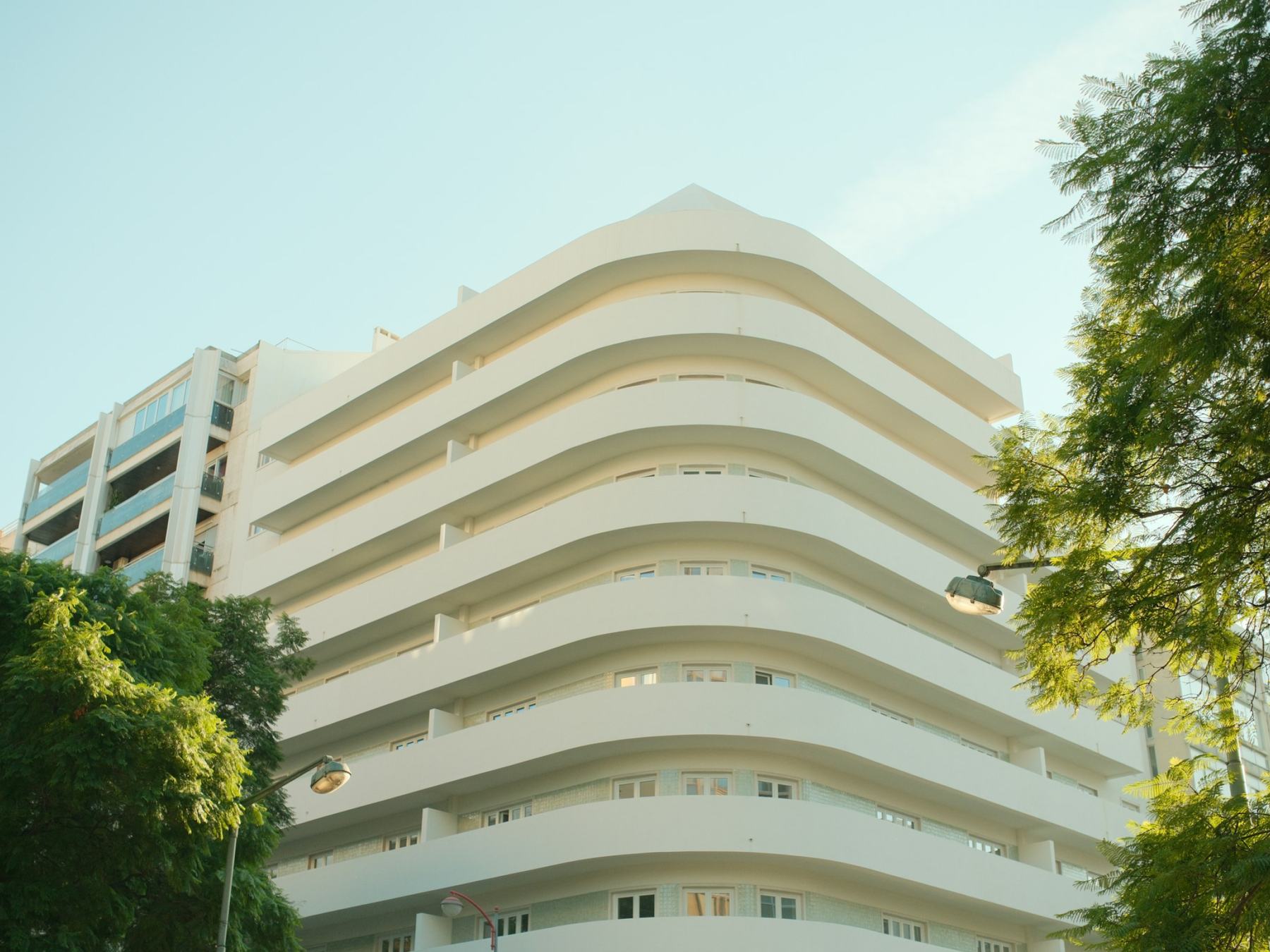 White residential building with curved balconies framed by trees in Lisbon